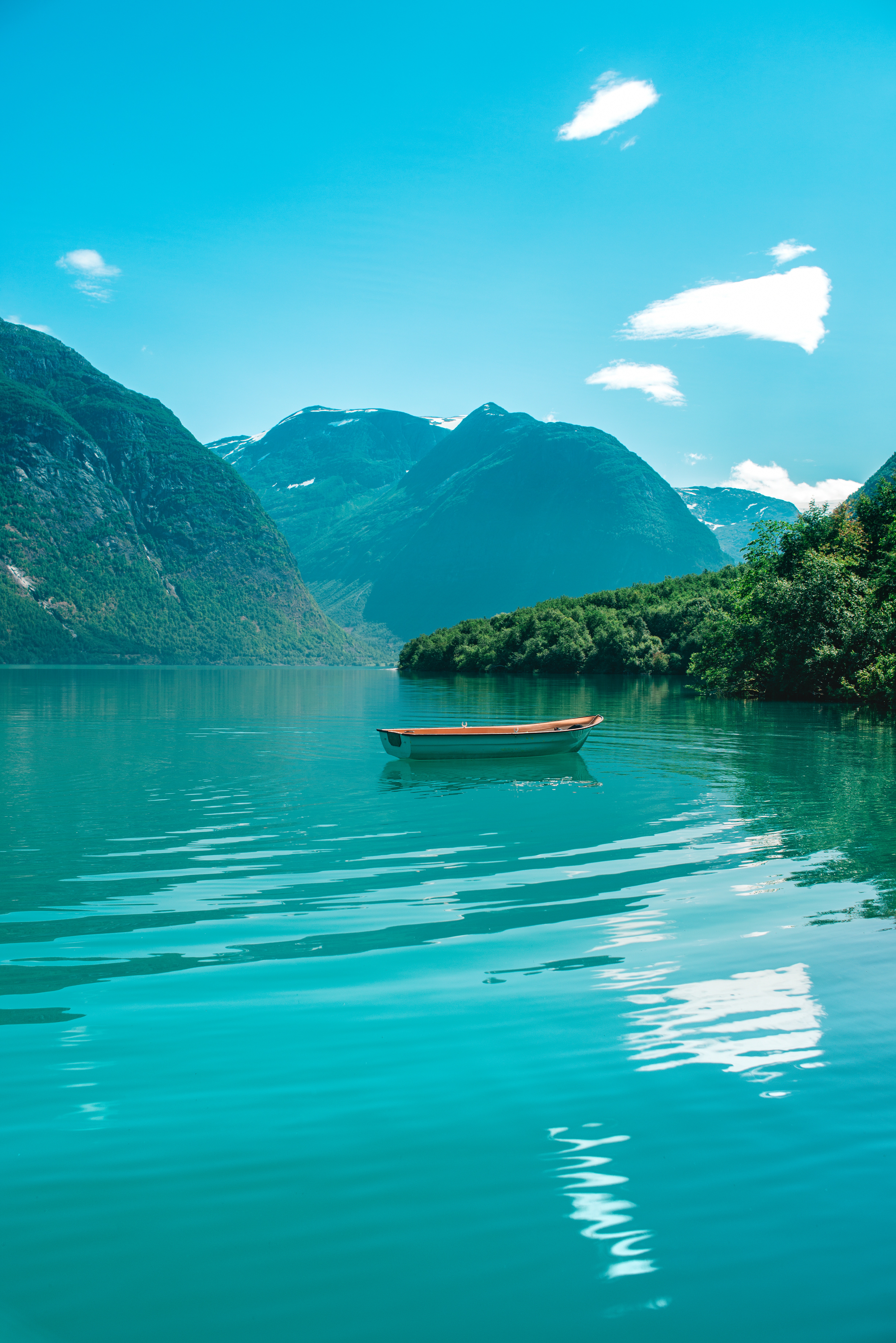 Turquoise mountain lake with a small boat surrounded by green mountains